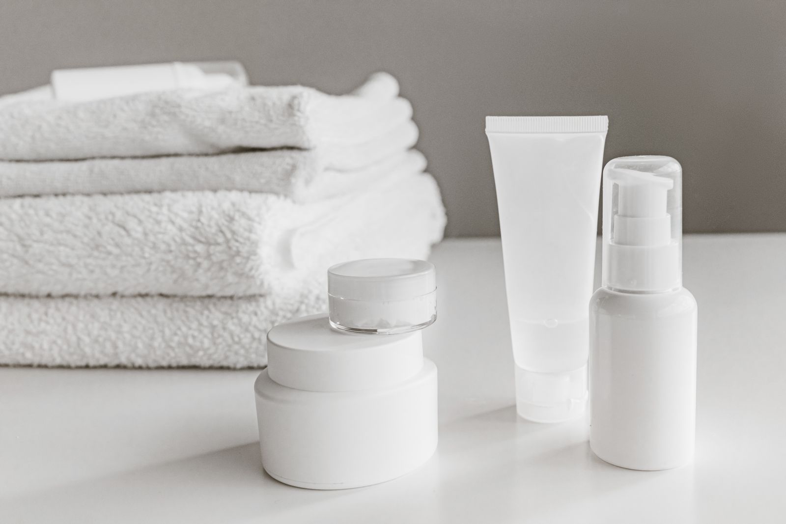 White skincare bottles and tubes beside folded towels
